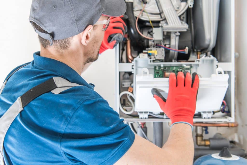 HVAC technician in protective gloves inspecting the internal electrical and control components of a furnace or heating system.